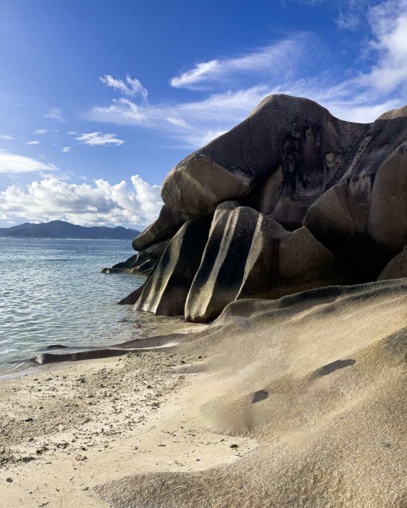 Smooth, weathered rocks on the beach in Seychelles under a clear blue sky.